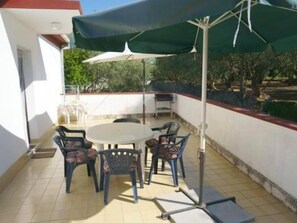Eine Terrasse im Freien mit einem runden Tisch, vier Stühlen, einem großen Sonnenschirm und einem Metallstiel.