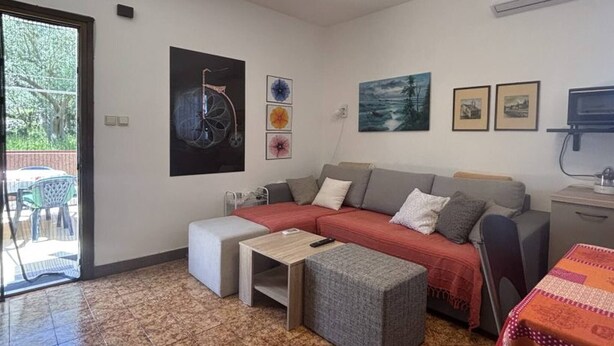 A modern living room with a sofa, ottoman, and a small table. There are framed pictures on the wall and a TV mounted on the wall. - 2 Bedroom Apartment Bor in Poljana (Preko)