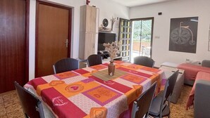 A dining area with a table covered in a patterned tablecloth, chairs, a vase with dried flowers, a bookshelf, and a door. - 2 Bedroom Apartment Bor in Poljana (Preko)