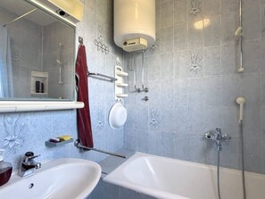 Ein Badezimmer mit einer Badewanne, einem Waschbecken, einem Spiegel, einem Handtuchhalter und einer Dusche.