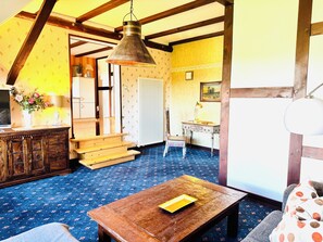 Una habitación con escalera de madera, un escritorio con lámpara, una mesa de madera con un libro y una alfombra azul estampada.