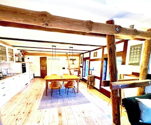 Un intérieur rustique avec une table à manger en bois, des chaises et un coin cuisine équipé de placards et d’une cuisinière.