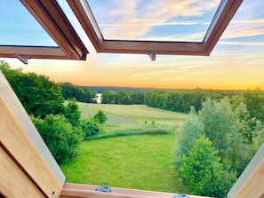 Una habitación con tragaluz, vistas a un campo verde y una lejanía arbolada.