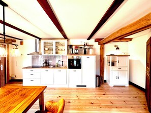 Una cocina funcional con vigas de madera, armarios blancos y una mesa de comedor.
