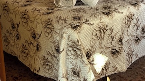 A bed with a floral-patterned bedspread, a rolled-up towel, and two pillows.