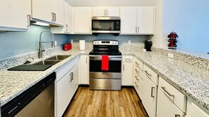 Una cocina moderna con electrodomésticos de acero inoxidable, armarios blancos y una encimera de granito.