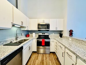 A modern kitchen with stainless steel appliances, white cabinetry, and a granite countertop. - King Suite on The Circle by Convention Center (Indianapolis)