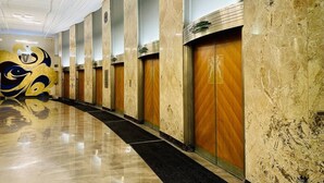 Un pasillo de hotel con paredes de mármol, puertas de madera y un suelo reflectante.