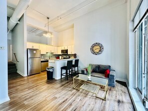 A modern kitchen with stainless steel appliances, a dining area with a glass coffee table, and a living room with a sofa and a decorative wall clock. - King Suite on The Circle by Convention Center (Indianapolis)