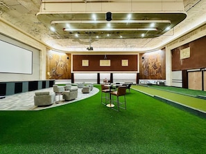 A conference room with artificial grass, seating, a projector screen, and a large wall mural. - King Suite on The Circle by Convention Center (Indianapolis)