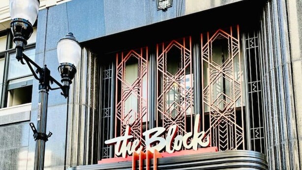 Un teatro con un cartel luminoso que dice 'the Block', ventanas amplias y fachada negra.