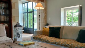 A living room with a sofa, a coffee table with cups, a lamp, and a bookshelf. - Large, cosy family home with swimming pool in the heart of the Perche region. (Perche en Nocé)