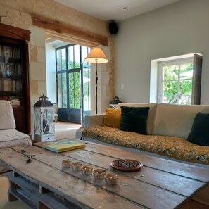 A living room with a sofa, a coffee table with cups, a lamp, and a bookshelf. - Large, cosy family home with swimming pool in the heart of the Perche region. (Perche en Nocé)