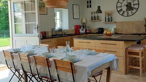 A modern kitchen with a dining area, featuring a large island, pendant lights, and a wall clock. - Large, cosy family home with swimming pool in the heart of the Perche region. (Perche en Nocé)