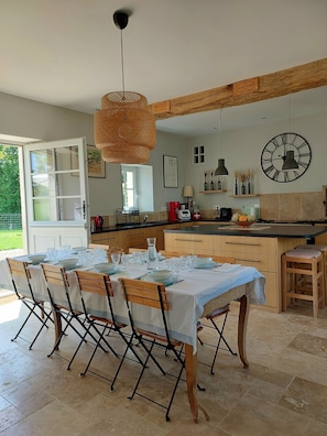 A modern kitchen with a dining area, featuring a large island, pendant lights, and a wall clock. - Large, cosy family home with swimming pool in the heart of the Perche region. (Perche en Nocé)