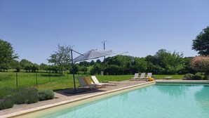 A swimming pool with lounge chairs and a shaded area. - Large, cosy family home with swimming pool in the heart of the Perche region. (Perche en Nocé)
