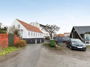 Eine Wohnstraße mit Häusern, einem Auto und einer grünen Tonne.