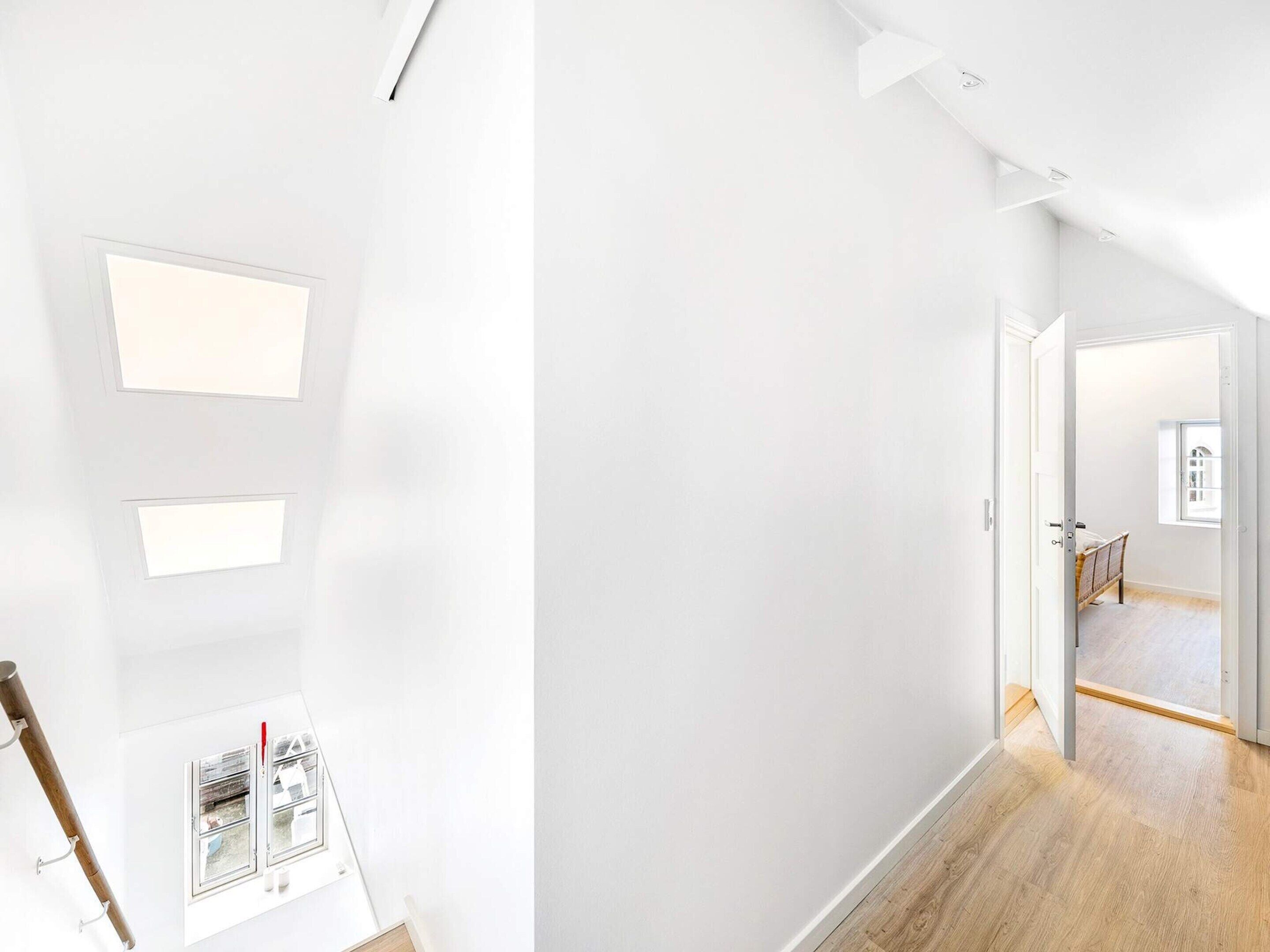 Un intérieur moderne avec des murs blancs, un plancher en bois et une porte visible donnant sur une autre pièce.