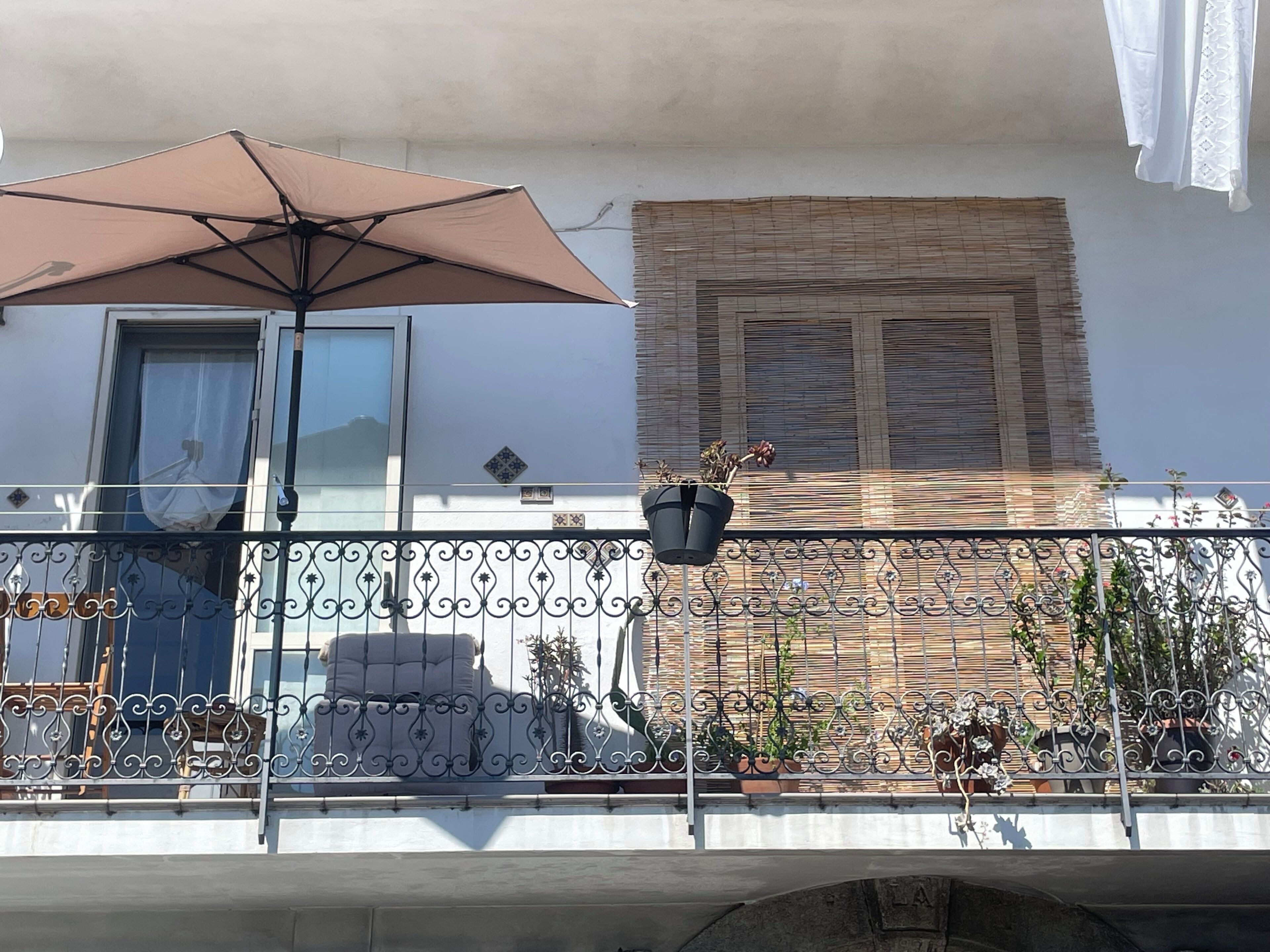 A balcony with a metal railing, a potted plant, and a beige umbrella.