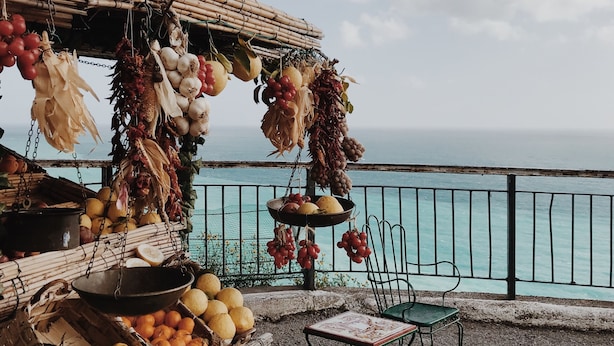 A seaside market stall with various fruits and vegetables, a chair, and a view of the ocean. - CasaElia | Path of the Gods & Amalfi Coast (Pianillo)
