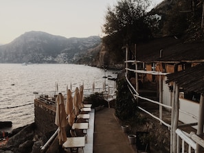 A seaside terrace with tables and chairs, overlooking a calm sea and distant mountains. - CasaElia | Path of the Gods & Amalfi Coast (Pianillo)
