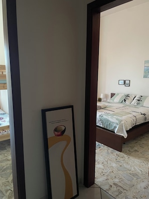 Une chambre à coucher avec un lit, une table de chevet, un tableau encadré et un sol carrelé.