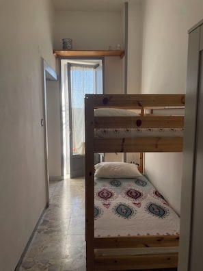 A bunk bed with a patterned bedspread, a wooden shelf above the bed, and a door leading to a bright room. - CasaElia | Path of the Gods & Amalfi Coast (Pianillo)