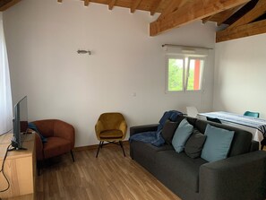 Ein Wohnzimmer mit einer Couch, einem Sessel, einem Fernseher und einem Fenster.