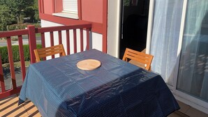 Un balcón con una mesa, sillas, barandilla roja y una puerta corrediza de vidrio.