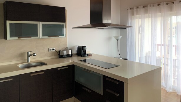 Una cocina moderna con horno empotrado, cafetera y un ventanal con cortinas.