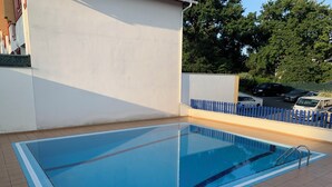Una piscina rectangular al aire libre con borde azul, rodeada por un patio de baldosas.