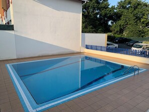 Ein rechteckiger Pool im Freien mit blauem Rand, umgeben von einer gefliesten Terrasse.