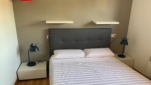 Una cama bien hecha con ropa de cama a rayas, dos mesitas de noche con lámparas y un cabecero tapizado en gris.