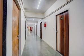 A long hallway with doors on both sides, a fire extinguisher mounted on the wall, and a number sign above one door.