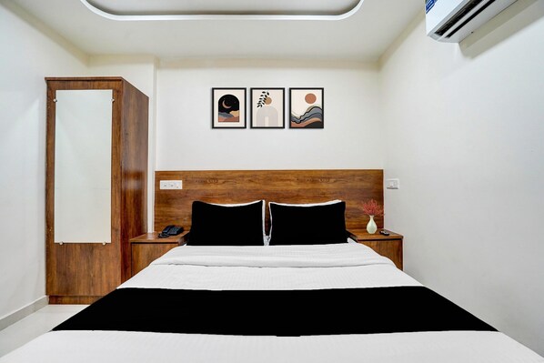 A hotel room with a wooden headboard, a bed with black and white bedding, a nightstand with a phone, and three framed artworks on the wall.
