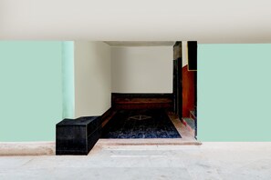 A narrow hallway with a black bench on the left and a red wall on the right. - Deluxe Aura Inn (Ahmedabad)