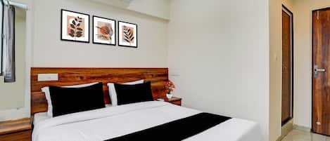 Habitación de hotel con cabecera de madera, una cama grande con ropa blanca, una mesita de noche con un jarrón de flores y cuadros en la pared.