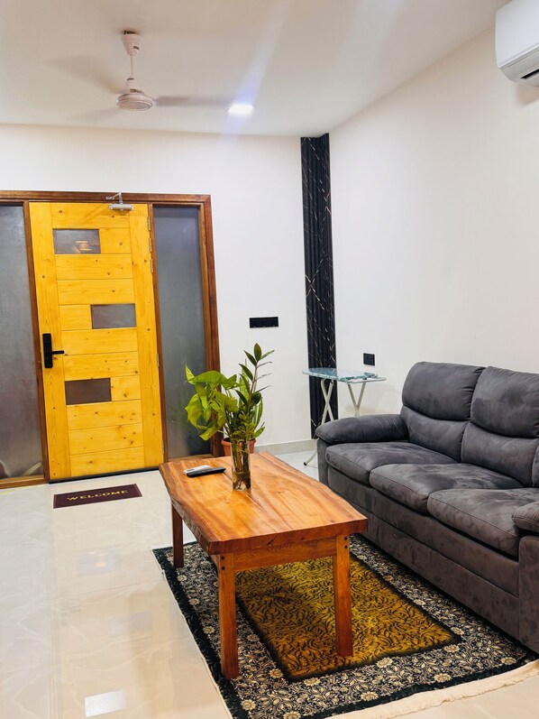 A living room with a sofa, a wooden coffee table with a plant, a door, and a ceiling fan.