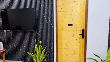 Quarto com parede revestida de painel acústico preto, porta de madeira com uma placa e duas plantas em vasos.