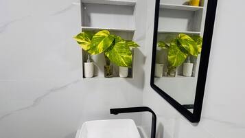Ein Badezimmer mit einem weißen Waschbecken, einem schwarzen Wasserhahn und zwei Blumentöpfen auf Regalen.