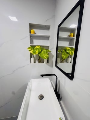 Ein Badezimmer mit einem weißen Waschbecken, einem schwarzen Wasserhahn und zwei Blumentöpfen auf Regalen.