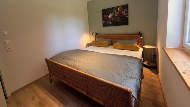 Un dormitorio con una cama grande, una mesita de noche, una lámpara de pared y un cuadro.