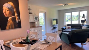 Comedor con una mesa dispuesta para dos, un televisor al fondo y un ventanal con vista a la vegetación.