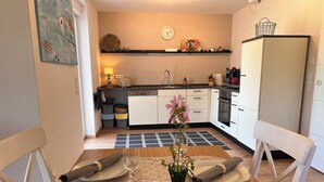 Un comedor con una mesa dispuesta para dos personas, un florero con flores, una vela y un reloj en la pared.