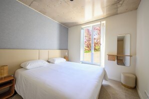 A modern bedroom with a large bed, a bedside table, a nightstand, a window with a view of trees, and a wall-mounted mirror. - Gorgeous 3-bedroom house in São Martinho do Porto near the beach (São Martinho do Porto)
