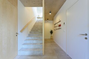 Escadaria que leva a um quarto com porta de madeira, planta em vaso e luminária na parede.
