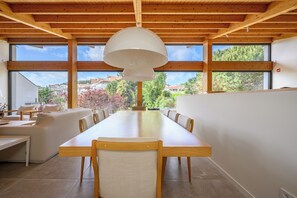 Un espace repas moderne avec une longue table en bois, des chaises et une grande fenêtre donnant sur des maisons et des arbres.
