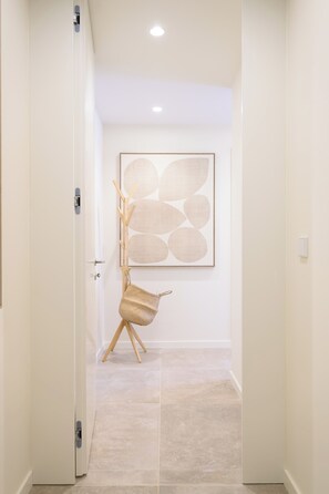 A hallway with a door, a wall-mounted abstract painting, and a woven chair. - Gorgeous 3-bedroom house in São Martinho do Porto near the beach (São Martinho do Porto)