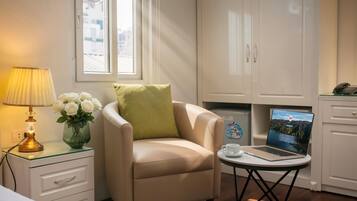 Una habitación con cama, una silla, un escritorio con una computadora portátil, una lámpara y un florero con flores.