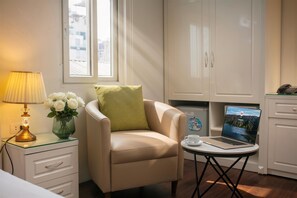 A room with a bed, a chair, a desk with a laptop, a lamp, and a vase with flowers. - Bastra Classy Hotel (Hanoi)